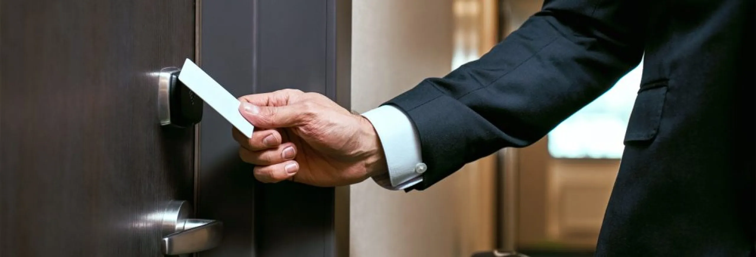 A hand unlocking a hotel door using a contactless RFID key card within a modern hospitality facility
