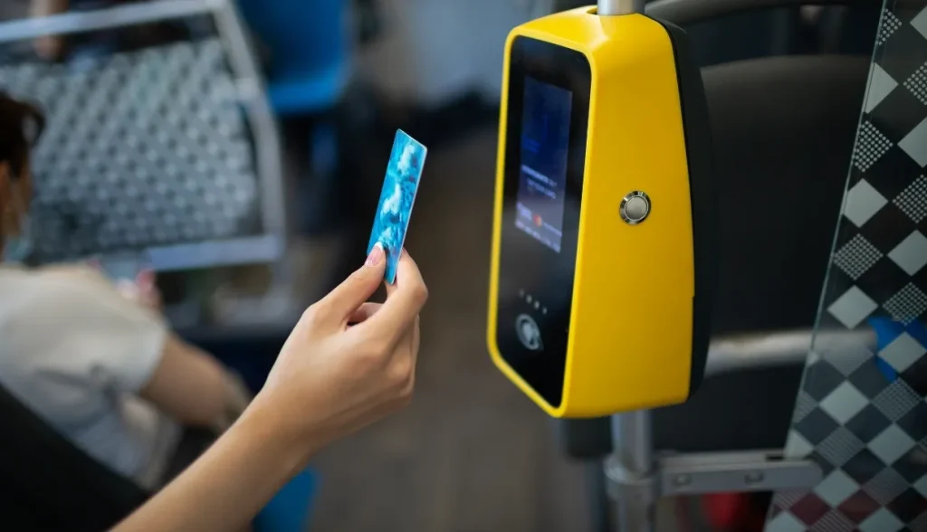 A passenger holding an RFID card near a yellow card reader on public transport.