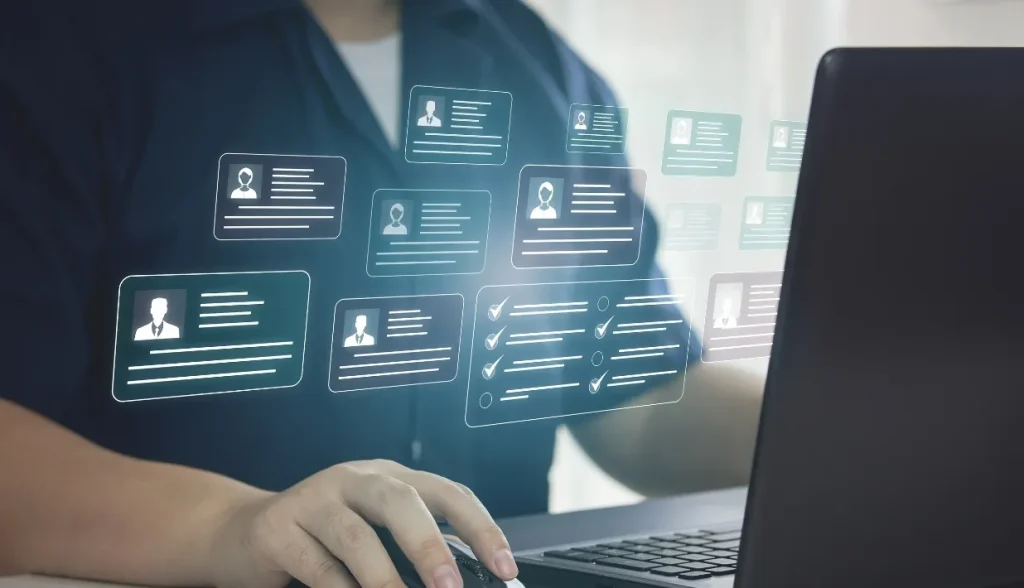 A person working on a laptop with multiple holographic digital cards floating above the keyboard, featuring user profiles and checklist icons, symbolizing data management and secure access control.
