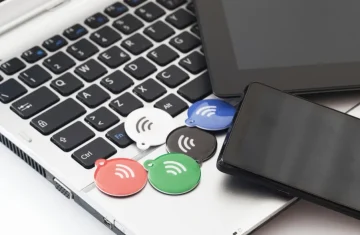 Colorful NFC key tags placed on a laptop keyboard next to a smartphone and tablet.