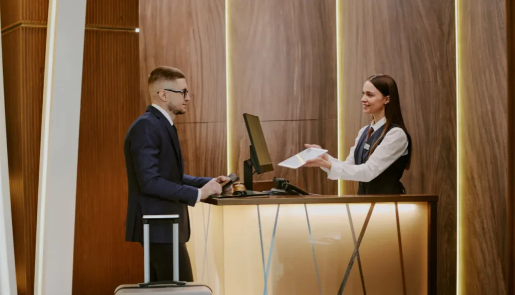 A hotel staff member at the front desk handing a document or card to a guest during check-in.