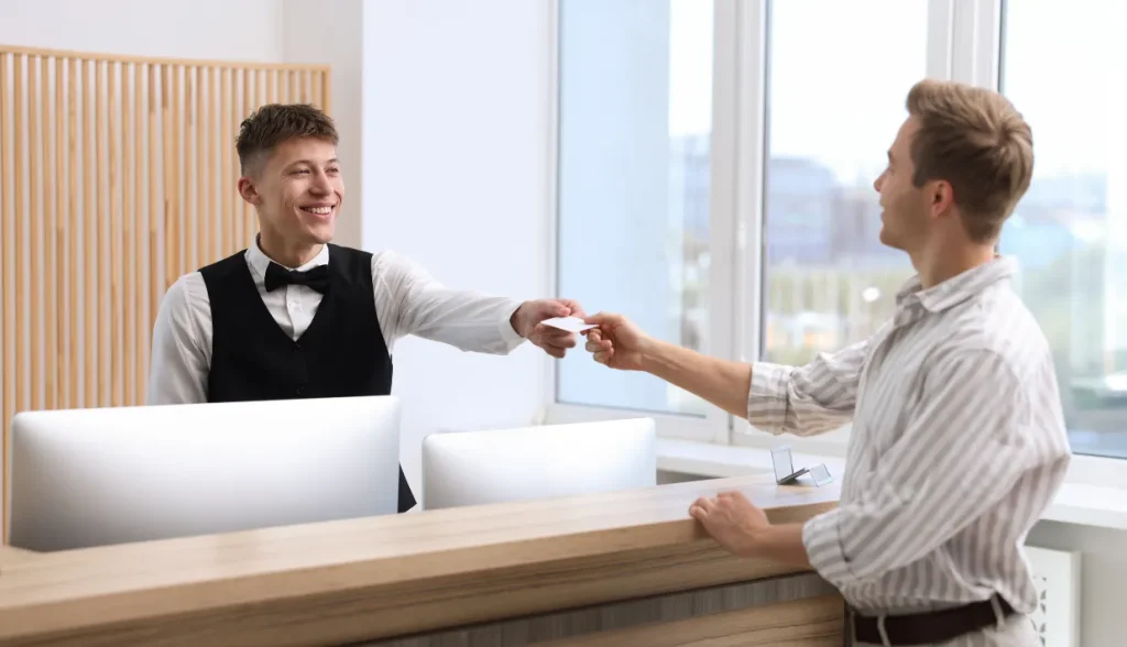 Smiling hotel front desk attendant handing an RFID key card to a guest at a modern check-in counter.