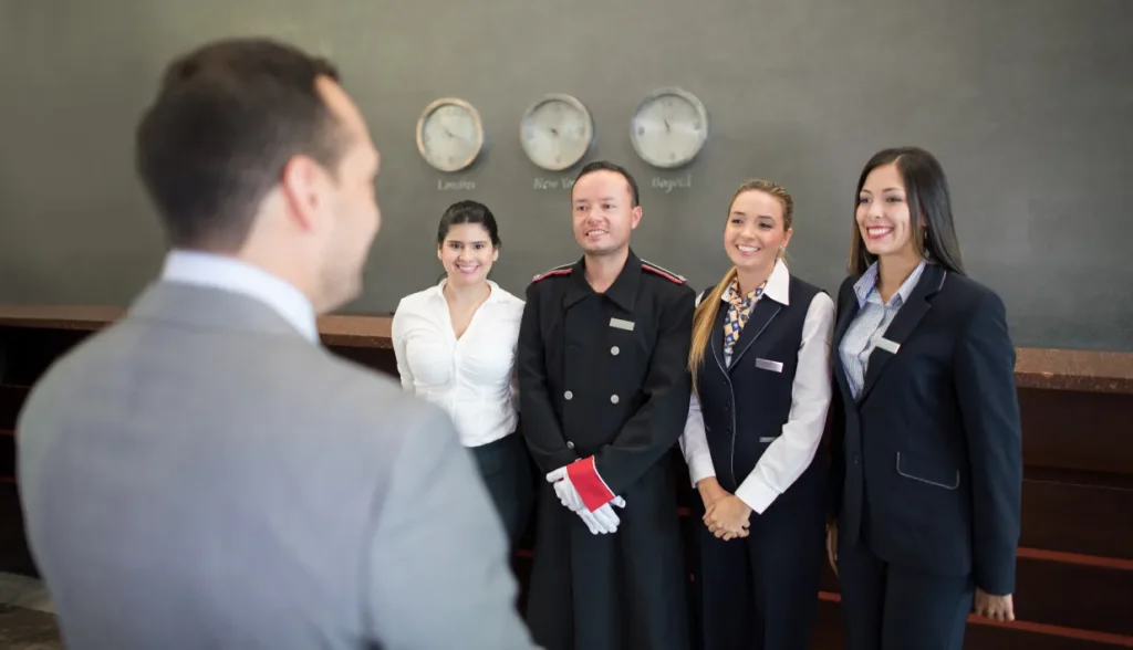 A group of hotel staff standing together for a briefing with a manager at the front desk.