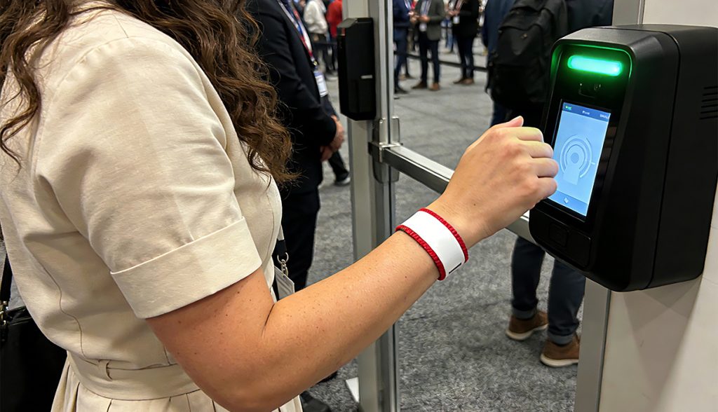 Woman tapping an RFID wristband on a contactless reader (with green light) for event entry, showing streamlined attendee experience.