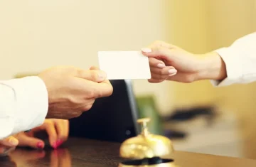 RFID Hotel Key Card Chips Explained Which MIFARE Chip Should Hotels Use Hotel front desk staff handing a blank RFID key card to a guest over a counter with a service bell.