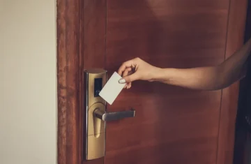 What RFID Chip Do Hotels Commonly Use for Key Cards Hand holding a white hotel key card near an RFID door lock on a wooden hotel door.