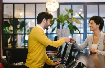 Why the Hospitality Industry Needs the Sustainable Key Card Hotel front desk staff handing a key card to a smiling guest in a modern lobby.