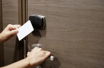 A person using a white RFID proximity card to unlock a door with a contactless reader, demonstrating access control.