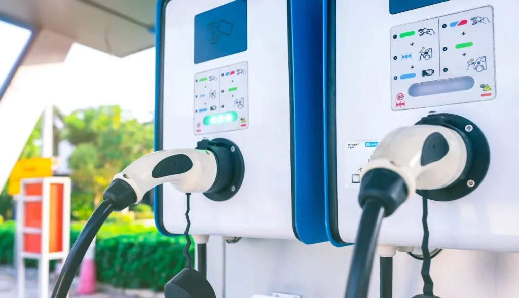 Close-up of a dual-port EV charging station with two connectors plugged in, showing interface icons and status lights.