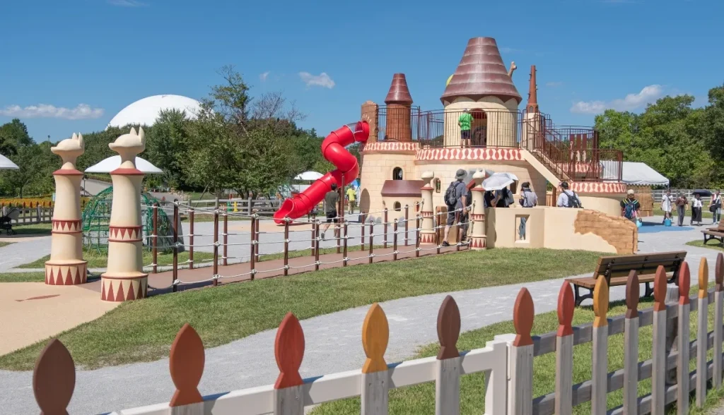 Whimsical outdoor playground with red slide, castle-like structure, and colorful fencing.