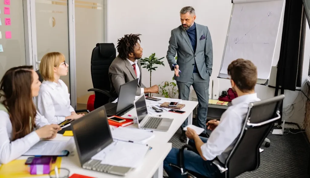 A hotel manager leading a team meeting around a whiteboard in a modern office.