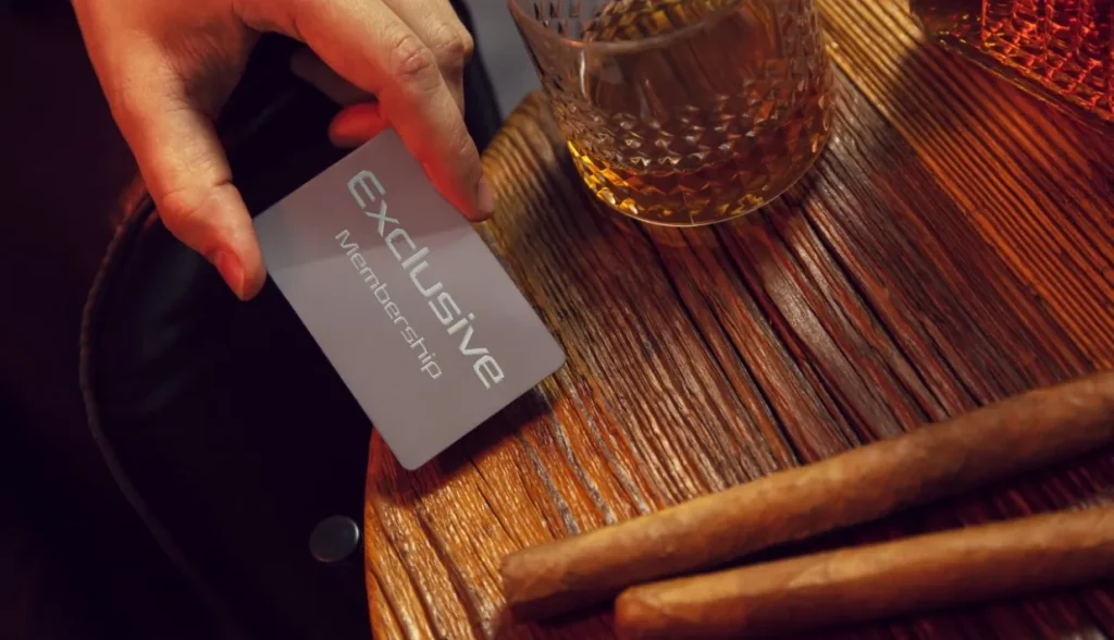 Premium "Exclusive Membership" card placed on a wooden bar with whiskey and cigars, representing a high-end RFID membership solution for smart spaces.