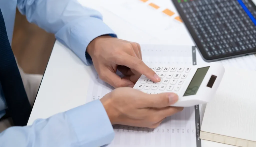 Close-up of hands calculating financial data with a calculator on spreadsheets and charts.