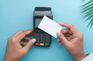 Do RFID Credit Cards Need Protection The Truth About RFID Skimming Hand holding a blank contactless card near a black POS payment terminal, demonstrating a typical card transaction setup for RFID skimming education.