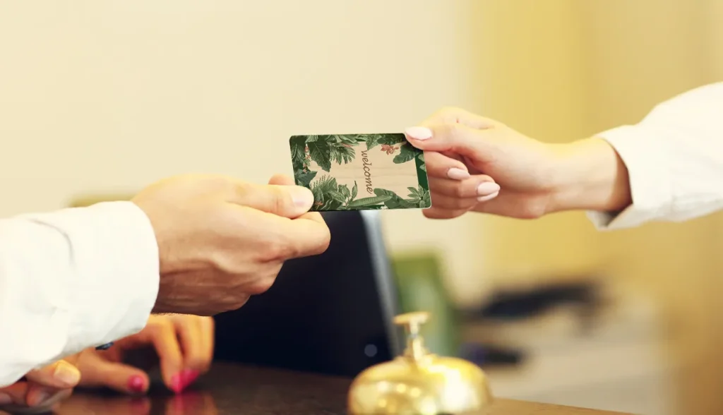 Hands exchanging a decorative wooden RFID welcome card at a hotel reception desk.