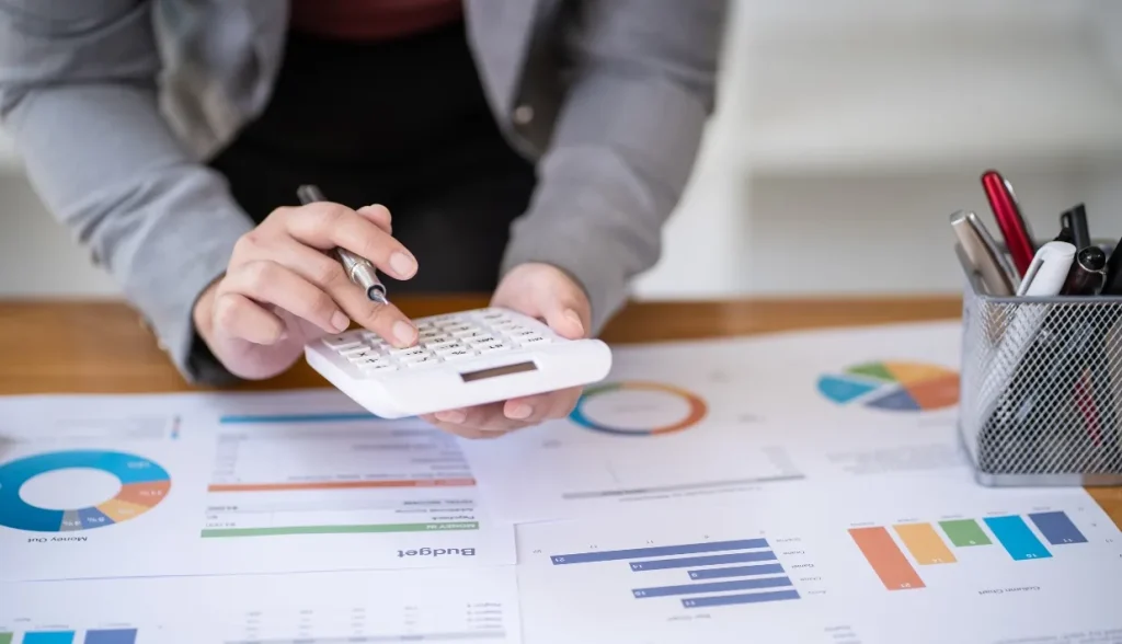 Hand using calculator on financial charts and budget documents.
