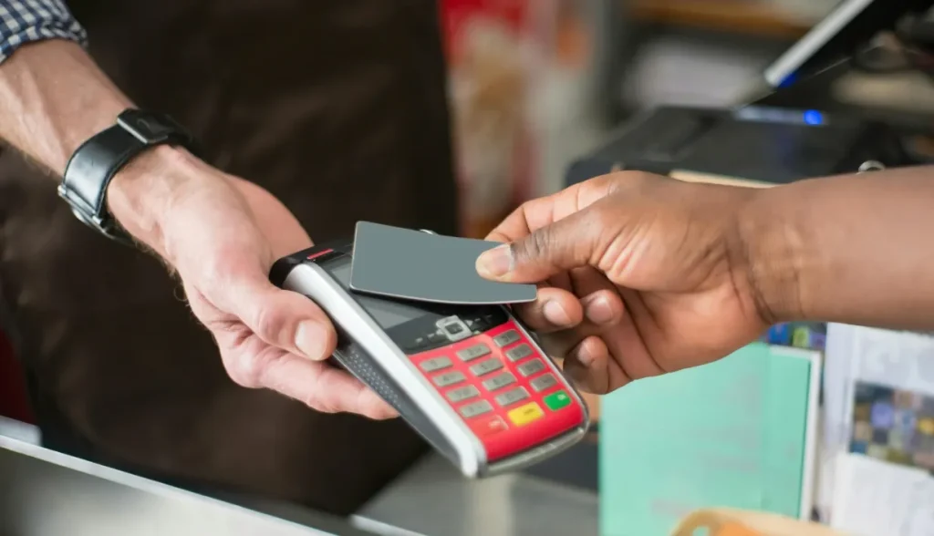 Person tapping credit card on POS terminal for contactless payment.