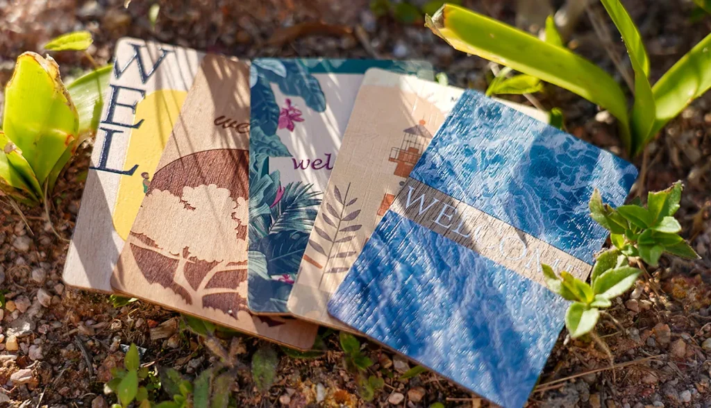 Assortment of decorative wooden RFID welcome cards placed outdoors among greenery.