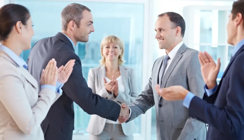 Business professionals shaking hands and celebrating a successful partnership in a bright office.